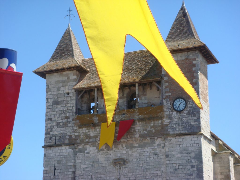 colourful banners flying in front of an old limestone building in a village in the south of France.